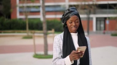 Sokakta akıllı telefon kullanan Müslüman bir kadın.