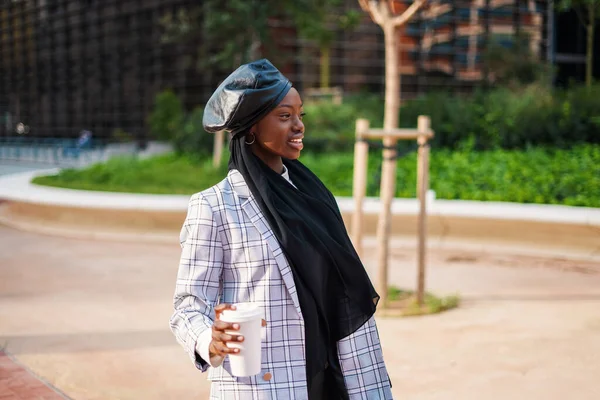 Mujer negra sonriente en bufanda y con café en el parque de la ciudad —  Fotos de Stock