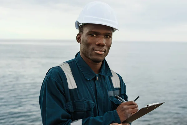 Black maritime worker making notes near sea — Stockfoto