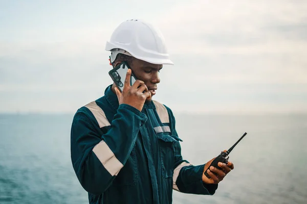 Black seaman with walkie talkie speaking on smartphone — Stockfoto