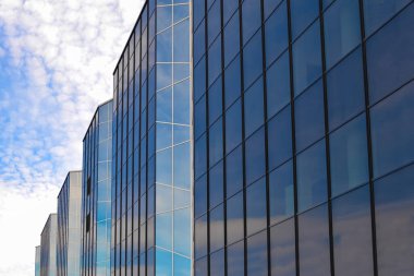 Mavi gökyüzüne ve bulutlara karşı camdan bir bina.