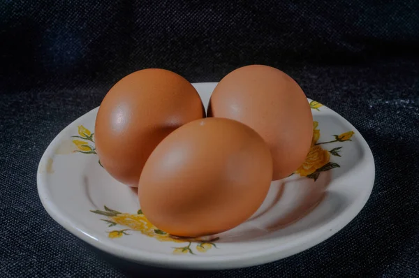 Drie Rauwe Kippeneieren Een Klein Bord Geïsoleerd Een Zwarte Achtergrond — Stockfoto