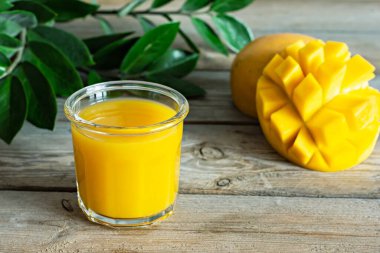 Bardakta taze mango suyu ve ahşap arka planda mango dilimi. Egzotik içki, yılın moda renkleri