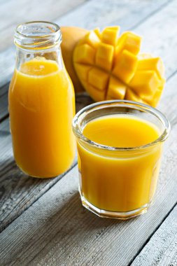 Bardakta taze mango suyu ve ahşap arka planda mango dilimi. Egzotik içki, yılın moda renkleri