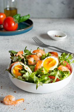Hafif arkaplanda beyaz bir tabakta sebzeli taze çıtır salata ve deniz ürünleri (karides). Sağlıklı gıda konsepti.