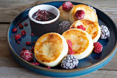 Taze süzme peynir veya taze böğürtlen ve reçelli mavi bir tabakta ricotta krepleri (şurup, börek). Nefis sağlıklı süzme peynirli kahvaltı. Ukrayna mutfağı, Rus mutfağı tatlı yiyecekler