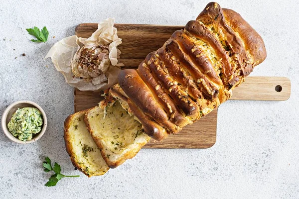 Homemade fresh  pull apart bread with herbs (parsley, thyme, rosemary, dill), garlic, cheese and spicy butter on a wooden board.