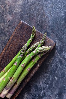 Koyu arkaplandaki tahta kesme tahtasındaki yeşil kuşkonmaz. Çiğ gıda konsepti, kopyalama alanı.