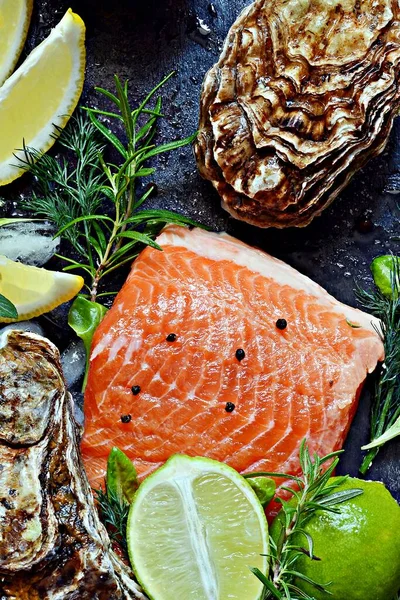 Taze istiridye, otlar, limon ve limonlu taze balık bifteği. Çiğ taze deniz ürünleri, narenciye ve baharatlar koyu bir arka planda..