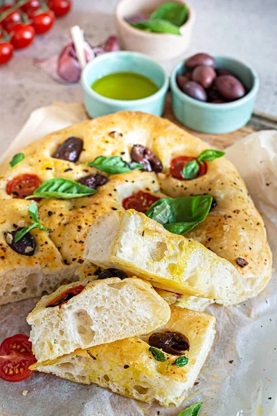Fresh Italian flat bread Focaccia with tomatoes, olives, garlic and herbs on a light background.