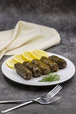 Koyu arkaplanda zeytinyağı ile doldurulmuş üzüm yaprakları. Geleneksel Türk mutfağı lezzetleri. Lezzetli dolma (yaprak sarma). Dikey görünüm. Kapat.