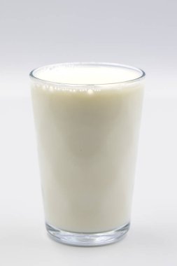 Beyaz arka planda bir bardak inek sütü. Yakın plan. Dikey görünüm