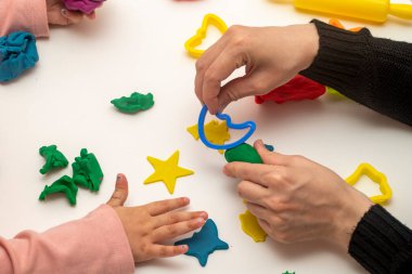 Annesiyle hamur oynayan bir kız. Anne ve kızı beyaz bir arka planda oynuyorlar. Hamurla çeşitli şekiller yapmak. Yakın plan. Anneler Günü