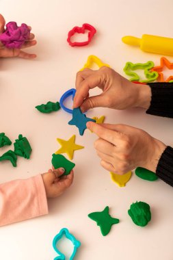 Annesiyle hamur oynayan bir kız. Anne ve kızı beyaz bir arka planda oynuyorlar. Hamurla çeşitli şekiller yapmak. Yakın plan. Anneler Günü
