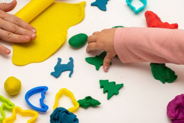 Annesiyle hamur oynayan bir kız. Anne ve kızı beyaz bir arka planda oynuyorlar. Hamurla çeşitli şekiller yapmak. Yakın plan. Anneler Günü