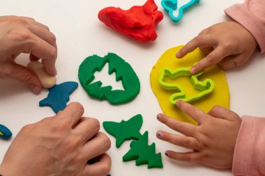 Annesiyle hamur oynayan bir kız. Anne ve kızı beyaz bir arka planda oynuyorlar. Hamurla çeşitli şekiller yapmak. Yakın plan. Anneler Günü