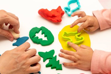 Annesiyle hamur oynayan bir kız. Anne ve kızı beyaz bir arka planda oynuyorlar. Hamurla çeşitli şekiller yapmak. Yakın plan. Anneler Günü