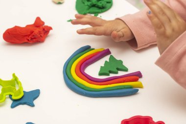 Hamur oynayan kız. Beyaz arka planda hamurlu gökkuşağı yapan kız. Hamurla çeşitli şekiller yapmak.