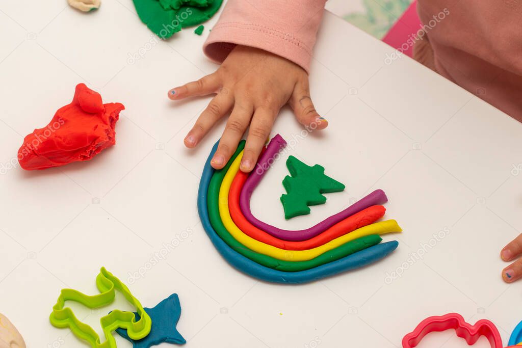 Girl playing dough. Girl making rainbow with dough on white background. Making various shapes with dough.