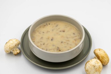 Beyaz arka planda mantar çorbası. Seramik tabakta taze yapılmış mantar çorbası. Yanında çiğ mantarla