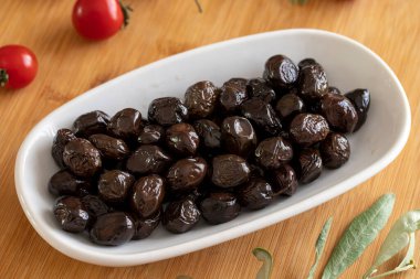 Siyah zeytin. Tabakta organik siyah zeytinler var. Ahşap arkaplanda siyah zeytin