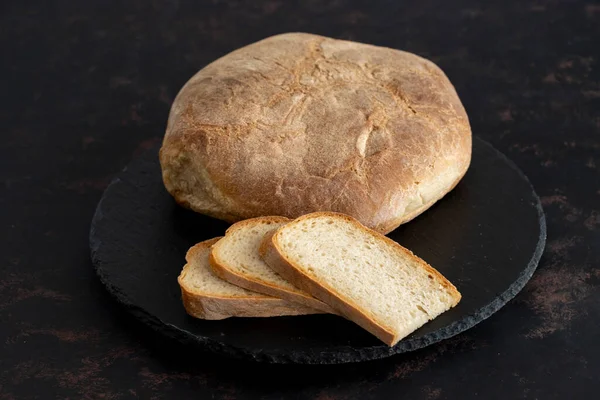 Organic round bread on a dark wooden background. Sliced bread. Traditional sourdough bread