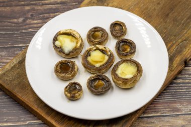 Ahşap bir zeminde seramik bir tabakta pişmiş mantar. Ekilmiş mantar veya portobello mantarı.