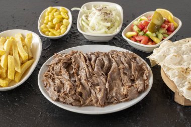 Koyu bir arka planda kebap. Geleneksel Türk mutfağı çeşnili et donörü. Lavaş ekmeği, patates kızartması, salata ve soğanlı.