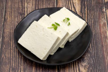 Tahta arka planda bitkilerle dilimlenmiş Feta peyniri. Yakın plan kahvaltı peyniri.