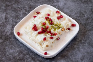 Arka planda Gullac tatlısı. Geleneksel Ramazan tatlısı. Şam fıstığı ve nar ile süslenmiş Gullac tatlısı. Türk mutfağı lezzetleri. Kapat.