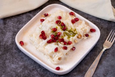 Arka planda Gullac tatlısı. Geleneksel Ramazan tatlısı. Şam fıstığı ve nar ile süslenmiş Gullac tatlısı. Türk mutfağı lezzetleri. Kapat.