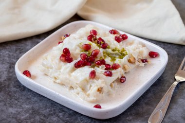 Arka planda Gullac tatlısı. Geleneksel Ramazan tatlısı. Şam fıstığı ve nar ile süslenmiş Gullac tatlısı. Türk mutfağı lezzetleri. Kapat.