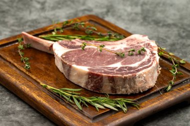 Esmer arka planda çiğ dana pirzolası. Tahta servis tahtasında çiğ dana pirzolası. Kapat.