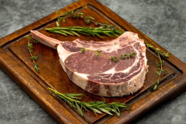 Esmer arka planda çiğ dana pirzolası. Tahta servis tahtasında çiğ dana pirzolası. Kapat.