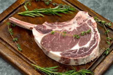 Esmer arka planda çiğ dana pirzolası. Tahta servis tahtasında çiğ dana pirzolası. Kapat.