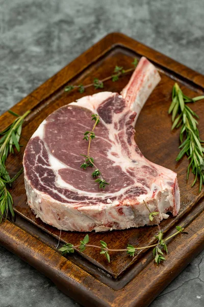 Esmer arka planda çiğ dana pirzolası. Tahta servis tahtasında çiğ dana pirzolası. Kapat.