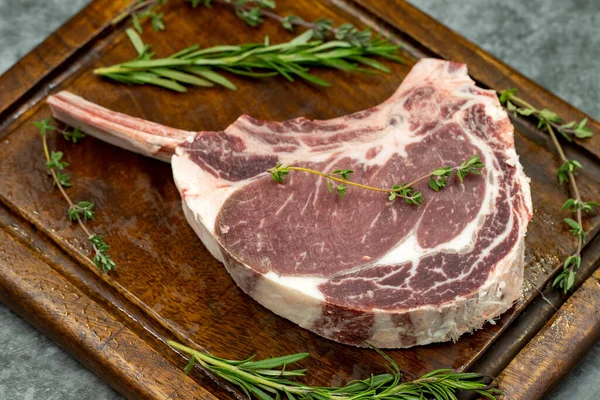 Esmer arka planda çiğ dana pirzolası. Tahta servis tahtasında çiğ dana pirzolası. Kapat.