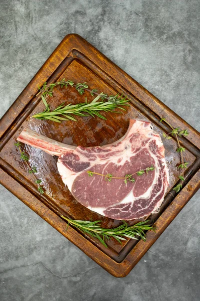 Esmer arka planda çiğ dana pirzolası. Tahta servis tahtasında çiğ dana pirzolası. Üst Manzara. Kapat.