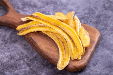 Kurutulmuş muz dilimleri. Karanlık bir arka planda dilimlenmiş kurumuş muz. Kurutulmuş meyve. Kapat.