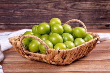 Ahşap zemin üzerinde yeşil erik. Sepette bir yığın yeşil erik. Kapat.