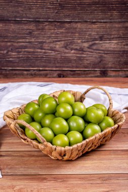 Ahşap zemin üzerinde yeşil erik. Sepette bir yığın yeşil erik. Kapat.