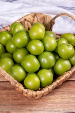 Ahşap zemin üzerinde yeşil erik. Sepette bir yığın yeşil erik. Kapat.