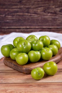 Ahşap zemin üzerinde yeşil erik. Tahta servis tabağında yeşil erik yığını. Kapat.