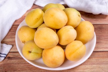 Ahşap arka planda kayısılar. Beyaz bir tabakta taze kayısı yığını. Kapat.