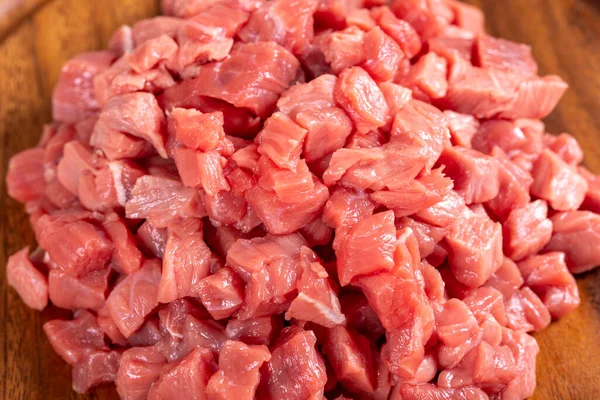 Cubed meat. Chopped red meat in a wooden serving dish on a stone background. Butcher products. close up