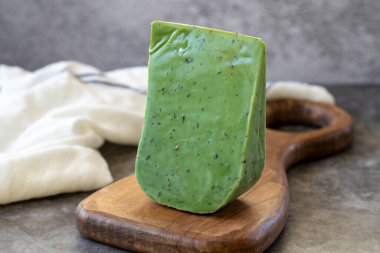 Green gouda cheese. Gouda cheese with basil on a dark background. Dutch cheese. close up