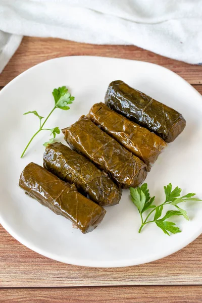 Wrapped leaves with olive oil on a wooden background. Traditional Mediterranean cuisine delicacies. Local name zeytinyagli yaprak sarma or dolmadika. close up