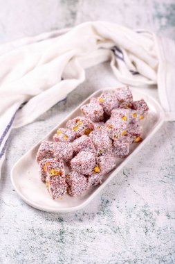 Nar aromalı Türk lokumu. Fıstıklı Türk Lokumu ve gri arka planda hindistan cevizi. Geleneksel Orta Doğu mutfağı lezzetleri. Kapat.