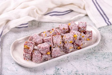 Nar aromalı Türk lokumu. Fıstıklı Türk Lokumu ve gri arka planda hindistan cevizi. Geleneksel Orta Doğu mutfağı lezzetleri. Kapat.