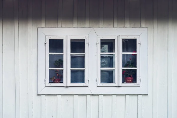 A detail of a white window against a white facade made of wooden planks. Country window